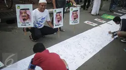 Seorang pria memegang poster sambil mengamati pengunjung Car Free Day (CFD) menandatangani spanduk berisi petisi mendukung kedatangan Raja Arab Saudi, Salman bin Abdulazis Al Saud, di Bundaran HI, Jakarta, Minggu (26/2). (Liputan6.com/Faizal Fanani)