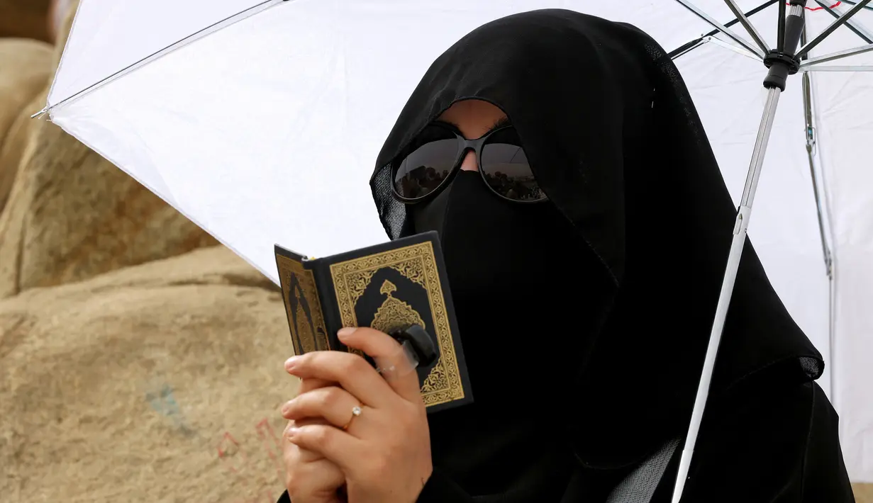 Jemaah haji membaca Alquran saat menunaikan prosesi wukuf di Padang Arafah, tenggara Kota Suci Mekah, Arab Saudi, Senin (19/7/2021). Ibadah haji tahun ini hanya diikuti oleh 60 ribu orang jemaah saja. (FAYEZ NURELDINE/AFP)