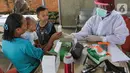 Bidan lengkap dengan baju Alat Pelindung Diri (APD) menjelaskan kegunaan obat kepada warga di Posko Imunisasi, Kelurahan Bakti Jaya, Tangerang Selatan, Senin (11/5/2020). Pada masa pandemi  Covid-19 pemberian vaksin atau imunisasi pada bayi sesuai jadwal. (Liputan6.com/Fery Pradolo)