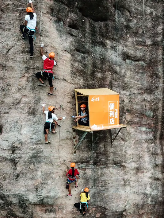 Seorang pemanjat tebing membeli air mineral di toko serba ada yang menempel di dinding tebing di Pingjiang di provinsi Hunan, China (25/4). Toko ini menjual minuman dan makanan untuk para pemanjat tebing yang melintas. (AFP Photo/China Out)