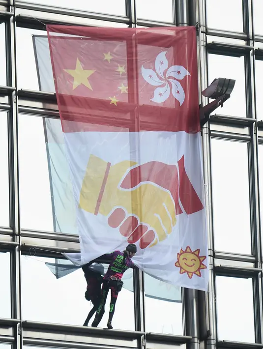 Alain Robert yang dijuluki 'French Spiderman' mengibarkan bendera China dan Hong Kong di Cheung Kong Center, Hong Kong, Jumat (16/8/2019). Alain membentangkan spanduk perdamaian ketika pusat bisnis itu mengalami masalah internal dan maraknya demonstrasi. (Lillian SUWANRUMPHA/AFP)
