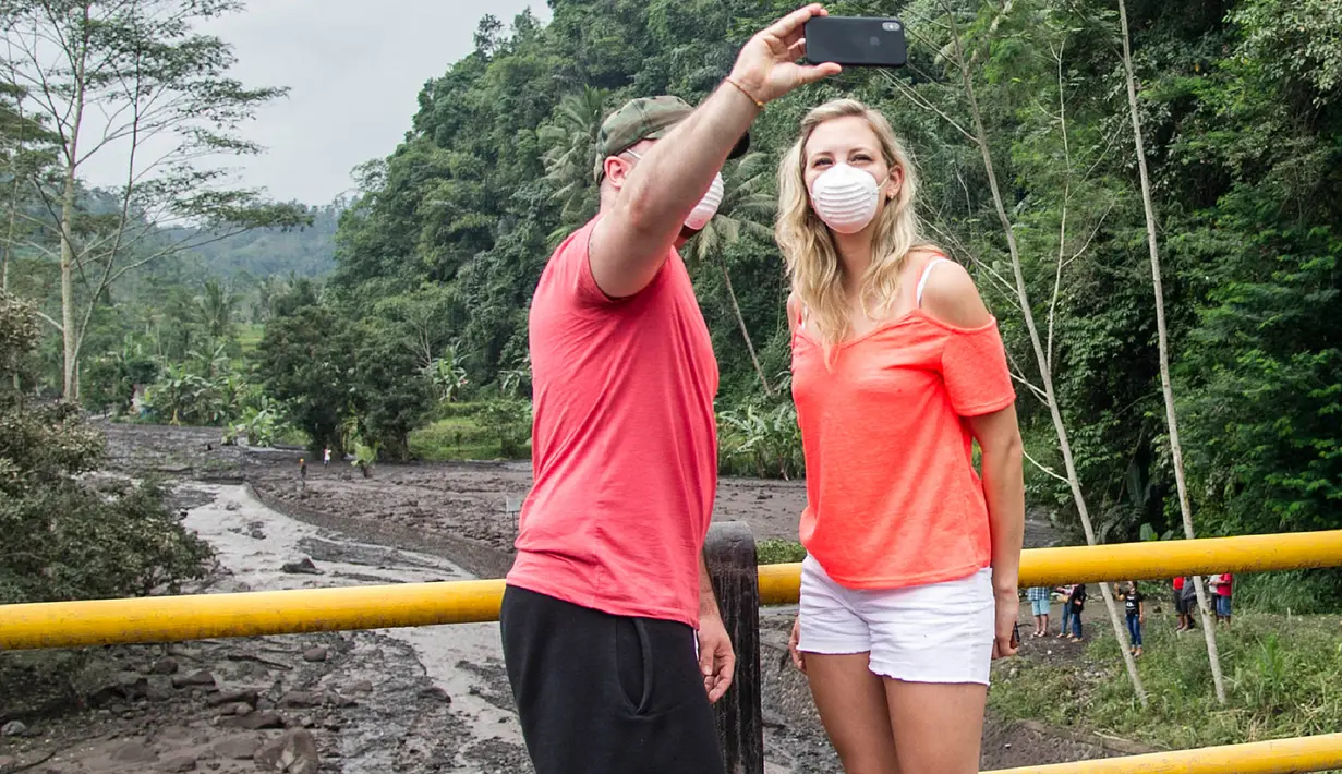 Turis berselfie dengan latar aliran lahar dingin Gunung Agung di Karangasem, Bali (29/11). Lahar dingin ini menyebabkan krisis air bersih di kawasan tersebut. (AFP Photo/Juni Kriswanto)