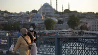 Wanita berjalan di atas Jembatan Galata dengan Masjid Suleymaniye di latar belakang, di Istanbul, Selasa (27/7/2021). Turki telah mencatat lebih dari 15.000 kasus virus corona baru, karena jumlah infeksi yang terus meningkat. (AP Photo/Mucahid Yapici)