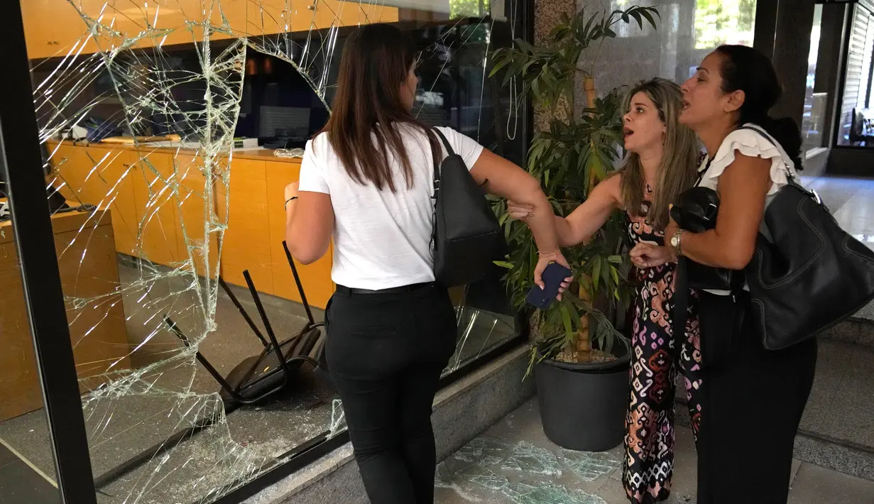 Karyawan bank yang panik berdiri di samping jendela yang dirusak oleh penyerang untuk keluar dari bank, Beirut, Lebanon, Rabu (14/9/2022). Menurut seorang saksi, dalam aksi pembobolan bank tersebut Sali Hafez memasuki bank bersama dengan aktivis dan menyerbu kantor manajer. (AP Photo/Hussein Malla)
