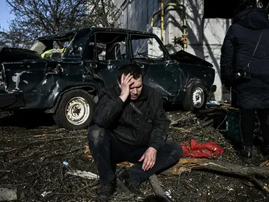 Seorang pria duduk di luar gedungnya yang hancur setelah pemboman di Kota Chuguiv, Ukraina timur, 24 Februari 2022. Angkatan bersenjata Rusia mencoba menyerang Ukraina dari beberapa arah, menggunakan sistem roket dan helikopter untuk menyerang posisi Ukraina di selatan. (Aris Messinis/AFP)