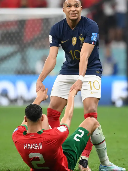 Penyerang Prancis #10 Kylian Mbappe membantu bek Maroko #02 Achraf Hakimi berdiri pada akhir babak semifinal Piala Dunia 2022 di Al Bayt Stadium, Kamis (15/12/2022) dini hari WIB. Tim berjuluk the blues menang 2-0 dari Maroko tanpa balas. (Photo by FRANCK FIFE / AFP)