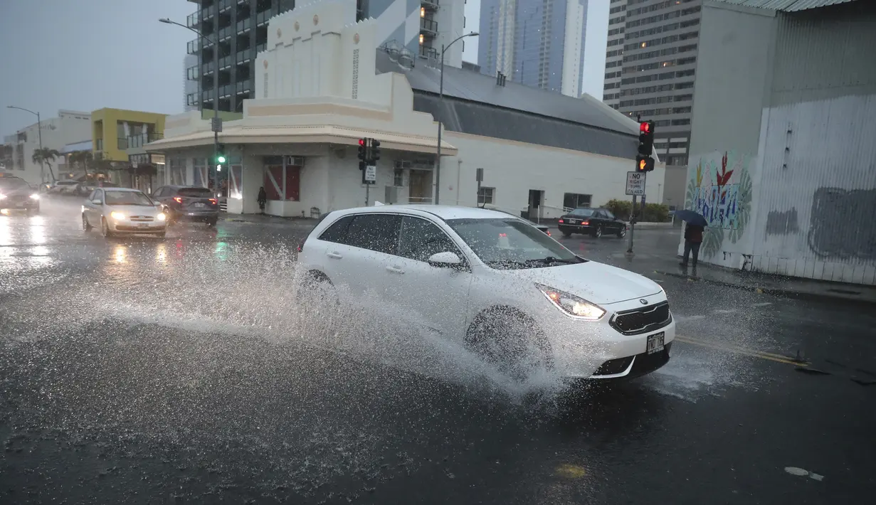 Sebuah mobil berbelok ke Cooke Street yang banjir di Honolulu (6/12/2021). Badai kuat yang membawa angin kencang dan hujan yang sangat deras membanjiri jalan-jalan dan meruntuhkan kabel listrik dan cabang-cabang pohon di seluruh Hawaii. (AP Photo/Marco Garcia)