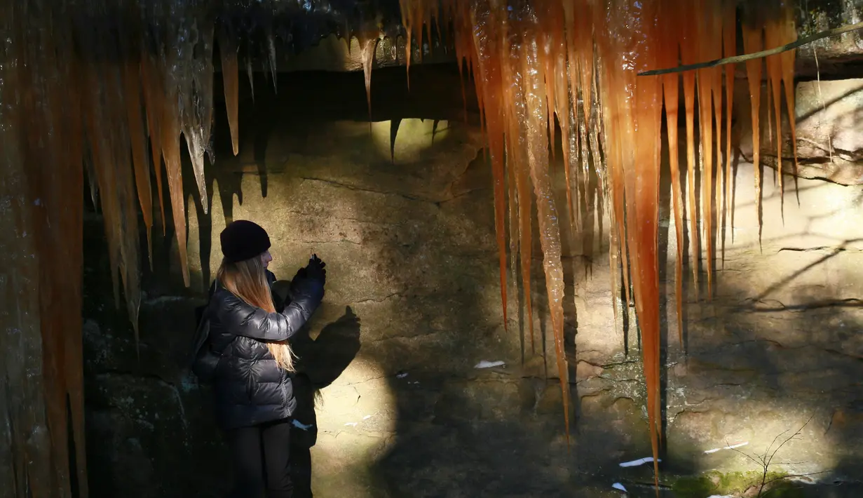 Pengunjung mengambil gambar air terjun oranye yang membeku di Desa Pulcin, Republik Ceko, Senin (23/1). Warna orange  tersebut disebabkan oleh ganggang yang hidup mikroskopis di dalam es. (AFP Photo/ RADEK MICA)