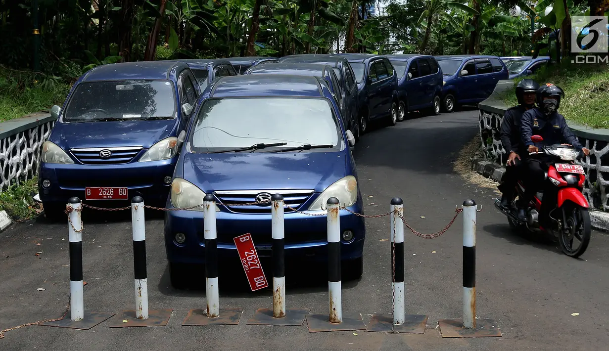 Pengendara motor melintasi deretan mobil dinas yang terparkir di area belakang Gedung DPR/MPR, Jakarta, Selasa (5/12).  Mobil-mobil berplat merah tersebut dibiarkan mangkrak hingga berkarat lantaran menunggu proses lelang. (Liputan6.com/Johan Tallo)