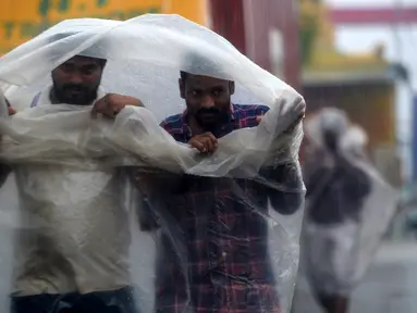 Dua pria menggunakan lembaran plastik untuk menutupi hujan lebat di Chennai saat topan Nivar mendekati pantai tenggara negara itu (25/11/2020). (AFP/Arun Sankar)