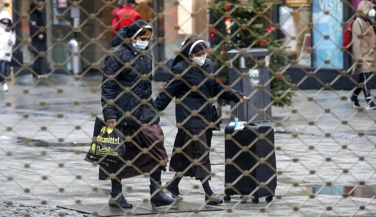 Dua biarawati terlihat berjalan dari balik pagar besi pusat perbelanjaan di Essen, Jerman, Senin (14/12/2020). Jerman melakukan lockdown nasional pada 16 Desember 2020 untuk memerangi pandemi COVID-19. (AP Photo/Martin Meissner)