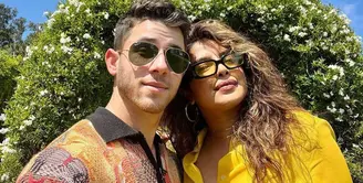 Pasangan Nick Jonas dan Priyanka Chopra merayakan Paskah dengan outfit bernuansa kuning. Priyanka memilih kemeja kuning polos, sedangkan Nick Jonas mengenakan sweater rajut berkerah dengan motif abstrak. Keduanya berpose selfie di depan dekorasi taman berbentuk telinga kelinci yang gemas. Foto: Instagram.