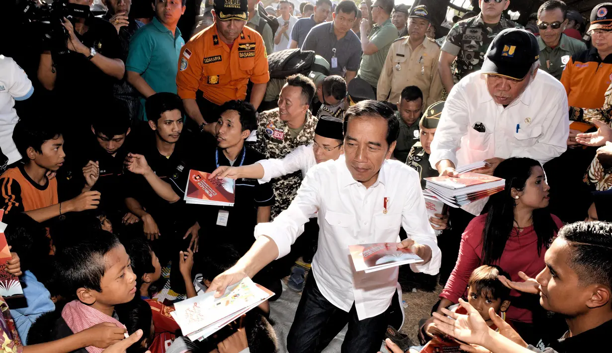 Presiden Joko Widodo atau Jokowi bersama Gubernur NTB Tuan Guru Bajang (TGB) Zainul Majdi membagikan buku saat mengunjungi korban gempa di lapangan Desa Madayin, Sambelia, Lombok Timur, NTB, Senin (30/7). (Agus Suparto/Indonesian Presidential Palace/AFP)