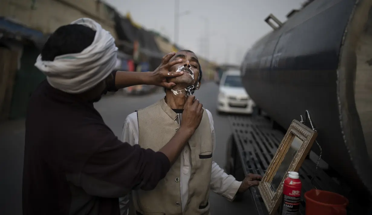 Seorang petani India melakukan pencukuran di lokasi protes di Ghazipur, pinggiran New Delhi, India, Kamis (9/12/2021). aksi mereka dengan memblokir jalan-jalan raya utama yang menghubungkan kota-kota terdekat dengan ibu kota negara tersebut. (AP Photo/Altaf Qadri)
