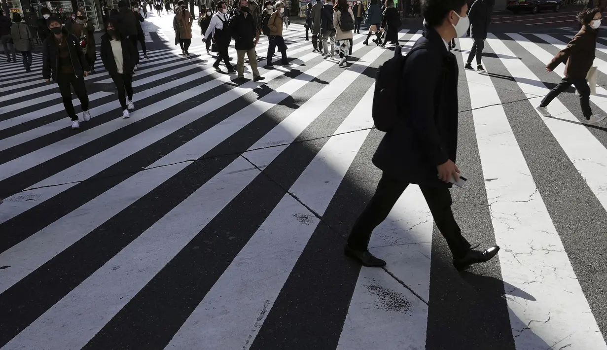 Orang-orang yang mengenakan masker pelindung untuk membantu mengekang penyebaran Virus Corona berjalan di sepanjang penyeberangan pejalan kaki di Tokyo (19/1/2021). Ibukota Jepang itu mengonfirmasi lebih dari 1.200 kasus Virus Corona baru pada 19 Januari 2021. (AP Photo/Eugene Hoshiko)