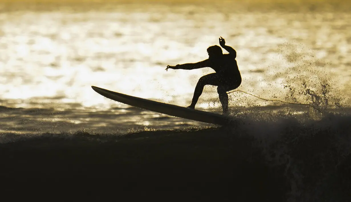 Seorang peselancar mengendarai ombak di Huntington Beach, California, Amerika Serikat, 12 Januari 2022. Peselancar di seluruh California Selatan berbondong-bondong ke daerah pantai saat gelombang ombak besar memasuki wilayah tersebut. (AP Photo/Ashley Landis)