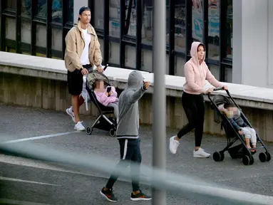 Cristiano Ronaldo bersama Georgina Rodriguez mendorong dua kereta bayi saat mereka berjalan-jalan dengan anak-anak mereka di Funchal pada 28 Maret 2020. Pesepakbola Cristiano Ronaldo dan kekasihnya, Georgina Rodriguez membagikan kabar duka. (AFP/HELDER SANTOS)