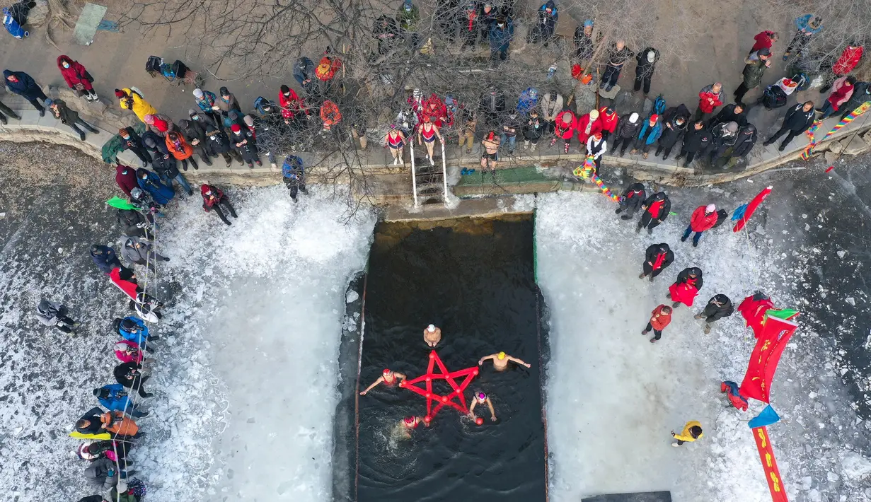 Foto udara yang diambil pada 25 Januari 2022 ini menunjukkan penggemar renang musim dingin menunjukkan bintang yang dibentuk dengan garis merah saat mereka berenang di danau yang sebagian beku di Shenyang, di provinsi Liaoning, China timur laut. (STR/AFP)