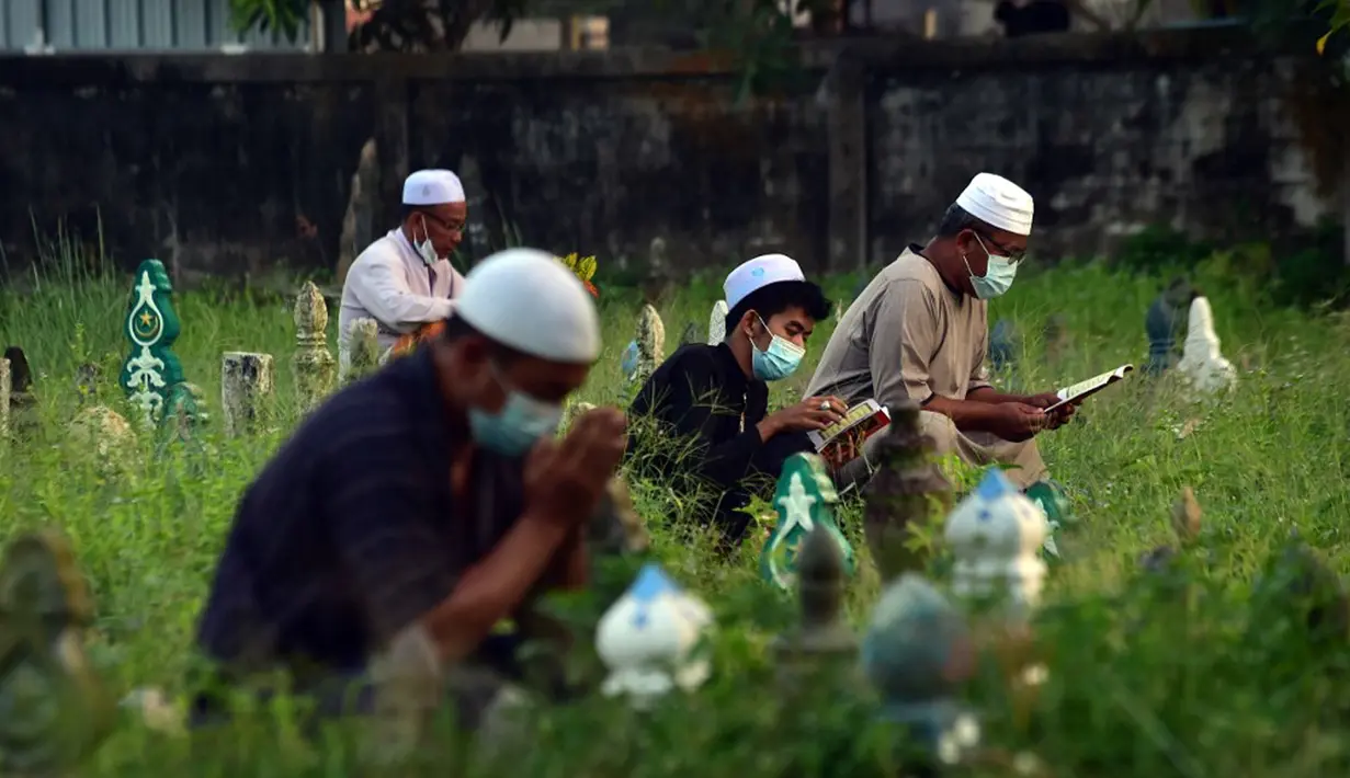 Orang-orang berdoa di sebelah makam kerabat saat perayaan Hari Raya Idul Adha di sebuah pemakaman di Provinsi Narathiwat, Thailand, Rabu (21/7/2021). Setiap Idul Adha atau hari besar Islam lainnya, sebagian warga banyak mendatangi kuburan untuk mendoakan keluarganya. (Madaree TOHLALA/AFP)