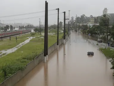 Sebuah kereta metropolitan terlihat di jalur rel yang banjir yang membentang di sepanjang sungai Pinheiros di Sao Paulo, Brasil, Senin, (10/2/2020). Hujan deras yang membanjiri kota, menyebabkan pinggir sungai utama meluap. (AP Photo/Andre Penner)