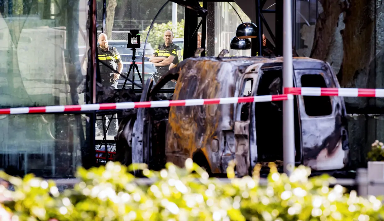 Petugas berdiri dekat mobil van yang menabrak pintu depan gedung tempat surat kabar ternama Belanda, De Telegraaf di Amsterdam, Selasa (26/6). Polisi kini tengah melakukan pencarian pelaku demi mengungkap motif di insiden itu. (KOEN VAN WEEL/ANP/AFP)