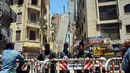 Aparat kepolisian menutup jalan dekat sebuah apartemen berlantai 13 yang mengalami kemiringan hingga mencapai blok apartemen lainnya di Alexandria, Mesir, Sabtu (3/6). Peristiwa itu memaksa polisi untuk mengevakuasi seluruh penghuni bangunan. (AP Photo)