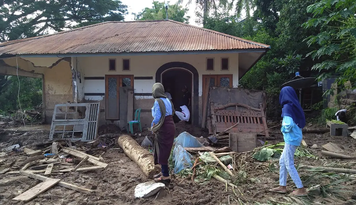 Para wanita berjalan melewati rumah yang rusak akibat banjir bandang di Waiwerang, Pulau Adonara, Nusa Tenggara Timur, Selasa (6/4/2021). Tim penyelamat terus menggali puing tanah longsor untuk mencari korban yang terkubur usai bencana banjir bandang. (AP Photo/Rofinus Monteiro)