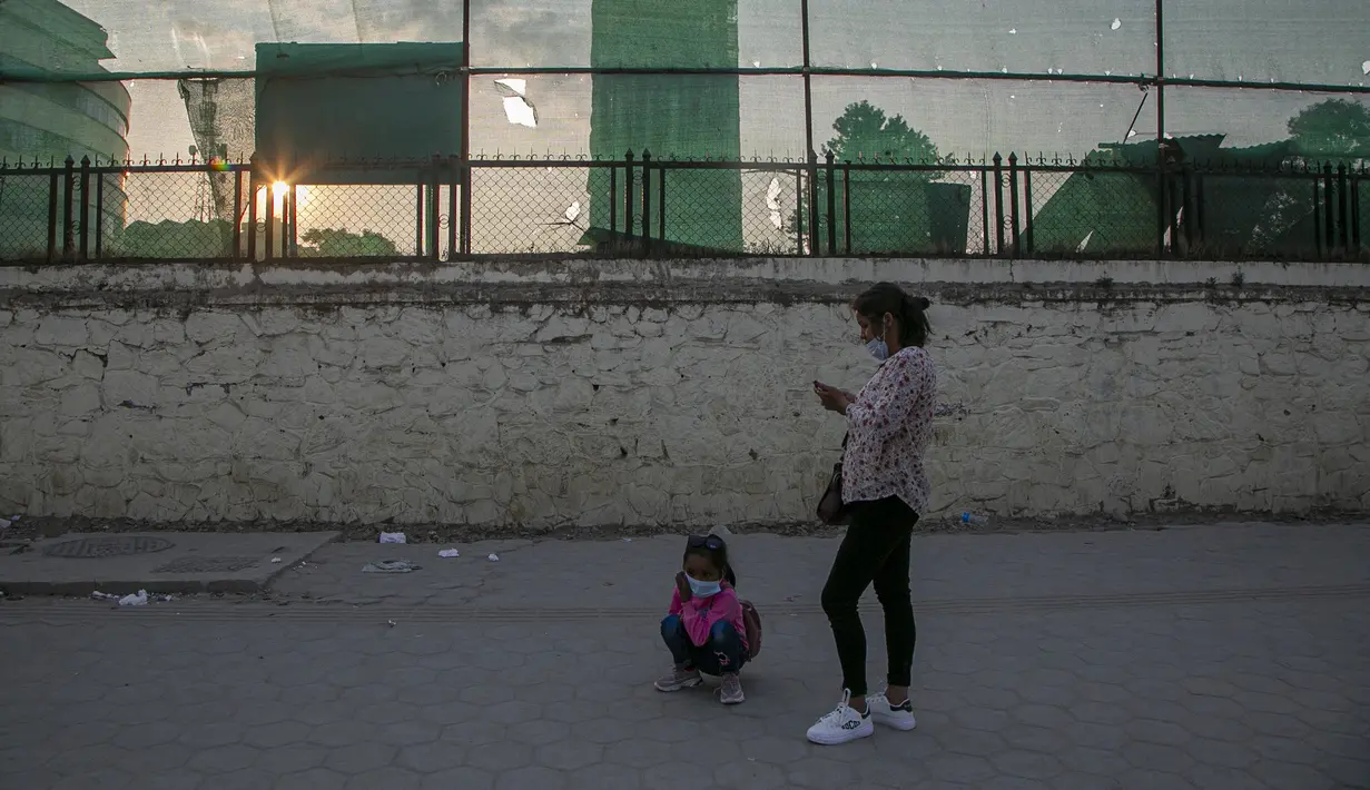 Seorang wanita dan putrinya yang mengenakan masker sebagai tindakan pencegahan terhadap virus corona COVID-19 menunggu angkutan umum di Kathmandu, Nepal, Selasa (13/10/2020). (AP Photo/Niranjan Shrestha)