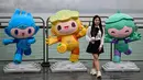 Seorang wanita berpose dengan maskot Asian Games 2022 (Chenchen, Congcong, dan Lianlian) di sepanjang jalur pejalan kaki sungai Qiantang di Hangzhou, provinsi Zhejiang, China pada 22 September 2023. (MANAN VATSYAYANA/AFP)