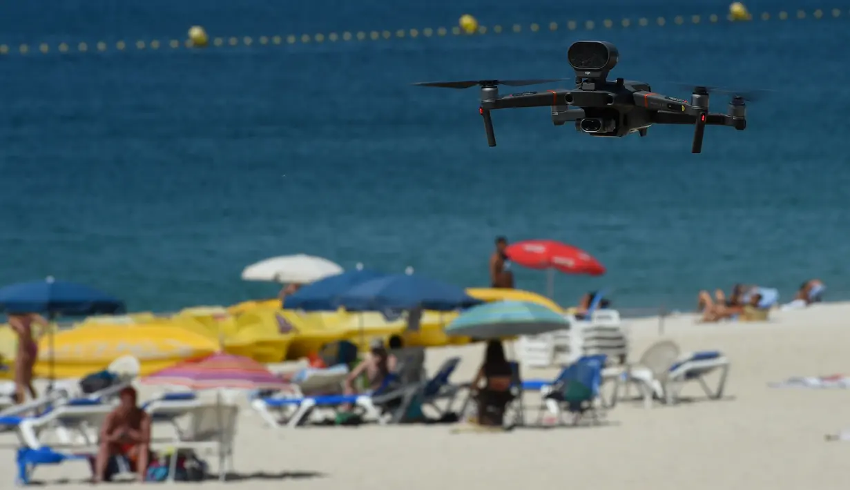 Sebuah drone atau pesawat tak berawak yang diterbangkan oleh polisi setempat memperingatkan orang-orang untuk menjaga jarak di pantai Areas di Sanxenxo, Spanyol, Selasa (14/7/2020). Drone tersebut untuk memantau jaga jarak antarwisatawan saat berlibur di masa pandemi Corona. (MIGUEL RIOPA / AFP)