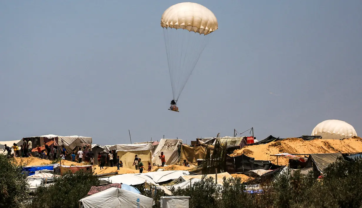 Terlihat benda-benda dengan parasut berjatuhan menuju ke tenda pengungsian warga Palestina. (Eyad BABA / AFP)