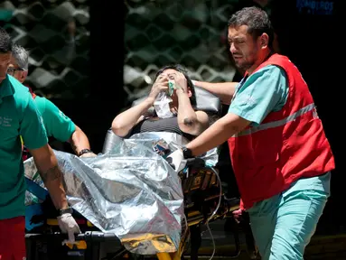 Seorang wanita dibawa ke ambulans setelah dievakuasi dari gedung perkantoran yang terbakar di pusat kota Buenos Aires, Argentina, Selasa (12/12/2023). (AP Photo/Natacha Pisarenko)