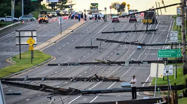 Pemandangan arah timur dari Route 97, seorang pria berdiri melihat tiang listrik yang tumbang di Route 140, Westminster, Maryland, Amerika Serikat, Selasa (8/8/2023). Tiang listrik bertumbangan setelah badai dahsyat melanda area tersebut pada Senin malam. (Jerry Jackson/The Baltimore Sun via AP)