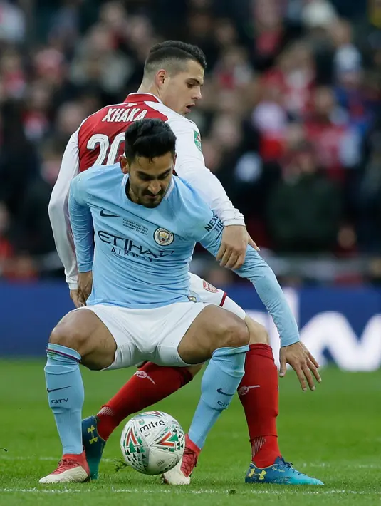 Pemain Arsenal, Granit Xhaka berebut bola dengan pemain dan kiper Manchester City, Ilkay Gundogan dalam laga final Piala Liga Inggris di Stadion Wembley, Minggu (25/2). Manchester City menghancurkan Arsenal dengan skor telak 3-0. (AP/Frank Augstein)