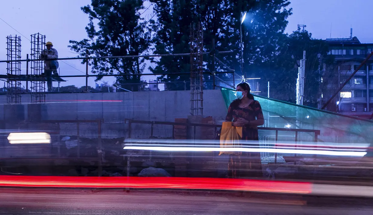 Seorang wanita yang mengenakan masker sebagai tindakan pencegahan terhadap virus corona COVID-19 menunggu taksi saat seorang pekerja konstruksi beristirahat di Kathmandu, Nepal, Selasa (13/10/2020). (AP Photo/Niranjan Shrestha)