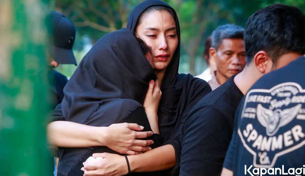Tyas berusaha untuk tegar menyaksikan prosesi pemakaman. Ia juga terlihat beberapa kali mengusap air mata.  Saling menguatkan, tampak Tyas memeluk seorang perempuan yang juga tak kuasa menahan tangis. [Foto: Muhammad Akrom Sukarya/KapanLagi.com]
