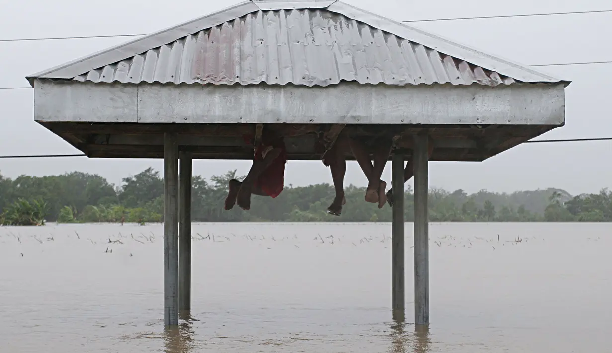 Warga bernaung di bawah atap salah satu halte bus jalan yang terendam banjir usai badai topan Linfa menghantam Luna, La Union, Filipina (6/7/2015). Badai tropis Linfa yang memiliki kecepatan 100 km per jam itu sedang bergerak ke utara. (REUTERS/TJ Corpuz)