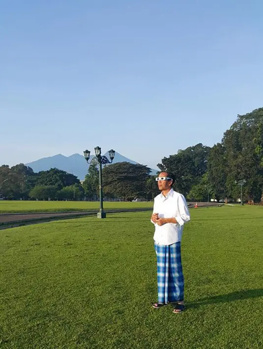 Dengan mengenakan kemeja putih dan sarung kotak-kotak berwarna biru, Jokowi tampak santai menyaksikan gerhana matahari di halaman Istana Bogor, Rabu (9/3). (facebook.com/Jokowi)