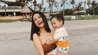 Vanessa Angel menggendong putranya, Gala Sky dalam momen liburan di sebuah pantai. (Instagram/@vanessaangelofficial)