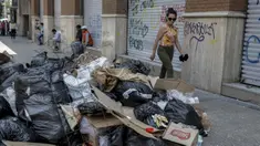 Seorang wanita berjalan melewati tumpukan sampah akibat pemogokan petugas sampah di Santiago (14/11/2019). Protes kekerasan meletus di ibukota Chile, Santiago, pada Selasa ketika mata uang negara itu turun ke level terendah dalam sejarah. (AFP/Javier Torres)