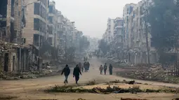 Sejumlah orang melintas di kawasan Salaheddine, Allepo Timur, Suriah (20/1). Pemandangan gedung hancur dan asap debu masih terlihat di kawasan ini. (AP/Hassan Ammar)