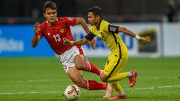 Bek Timnas Indonesia, Rachmat Irianto berusaha merebut bola gelandang timnas Malaysia, Mohamad Faisal Abdul Halim pada laga Grup B Piala AFF 2020 di Stadion Nasional Singapura, Minggu (19/12/2021). Hasil ini membuat timnas melangkah ke semifinal melawan Singapura. (AFP/Roslan Rahman)