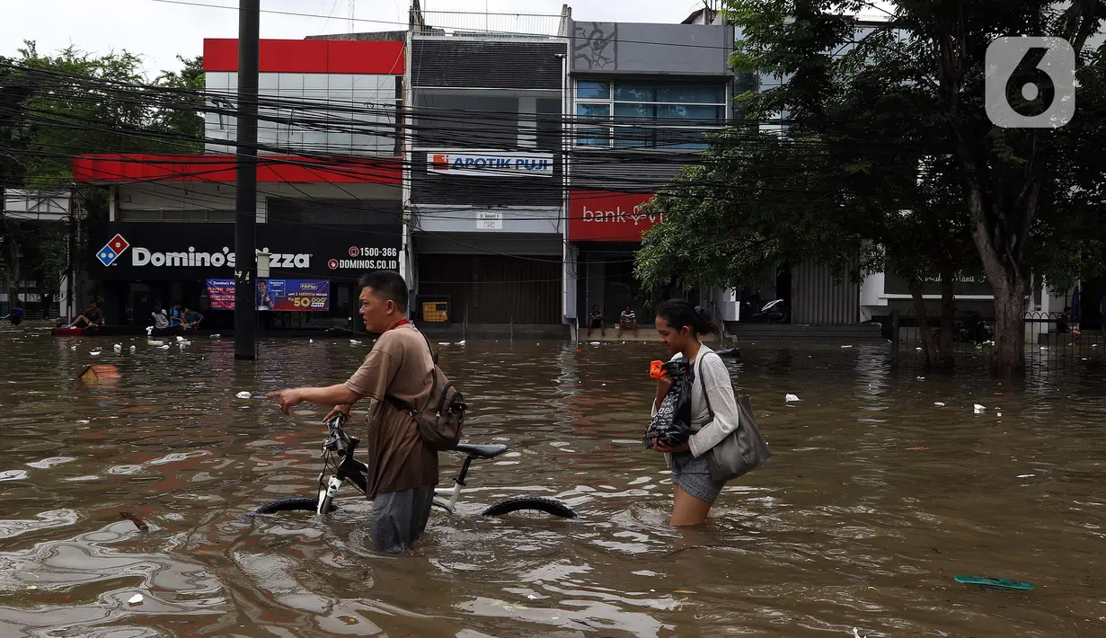 Warga melintasi banjir yang merendam kawasan Green Garden, Jakarta Barat, Selasa (25/2/2020). Hujan yang mengguyur kawasan Jakarta membuat kawasan tersebut tergenang banjir setinggi 60-80 cm. (Liputan6.com/Johan Tallo)