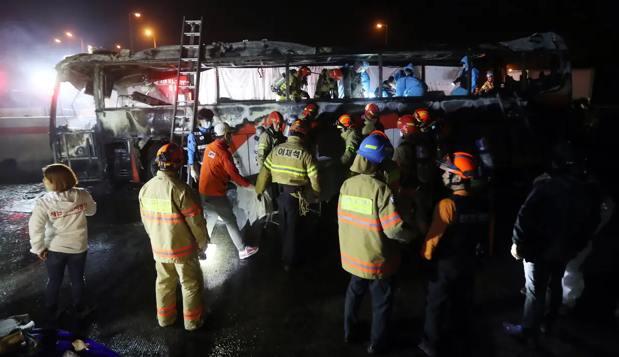 Petugas mencoba memadamkan bara api yang masih tersisa di badan bus  yang terbakar di Gyeongbu Expressway, tenggara Kota Ulsan, Korea Selatan, Jumat (14/10). Sedikitnya 10 orang tewas dan tujuh lainnya luka berat akibat insiden itu. (Yonhap/AFP)