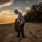 Tengku Mohamad Ali Mansor memeriksa botol kaca di sebuah pantai di desa Mangkuk, Malaysia timur pada 12 September 2020.  Upaya seorang lansia Malaysia untuk membersihkan pantai-pantai negara itu dari kaca-kaca yang terkelupas membuatnya mengumpulkan koleksi ribuan botol. (AFP/Mohd Rasfan)