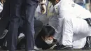 Rekaman NHK menunjukkan beberapa petugas polisi berseragam dan berpakaian preman berkumpul di sekitar pria tersebut, menekannya ke tanah dan menyeretnya ke samping. (Kyodo News via AP)