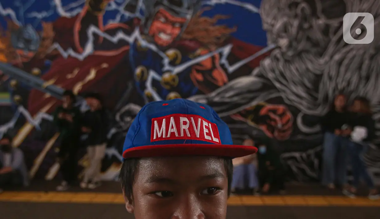 Seorang anak mengenakan topi Marvel berdiri dengan latar belakang mural kolaborasi di Terowongan Kendal, Kawasan TOD Dukuh Atas, Jakarta, Rabu (6/7/2022). Karya seni mural yang terinspirasi dari film Marvel Studios "Thor: Love and Thunder" itu memanfaatkan teknologi augmented reality (AR). (Liputan6.com/Faizal Fanani)