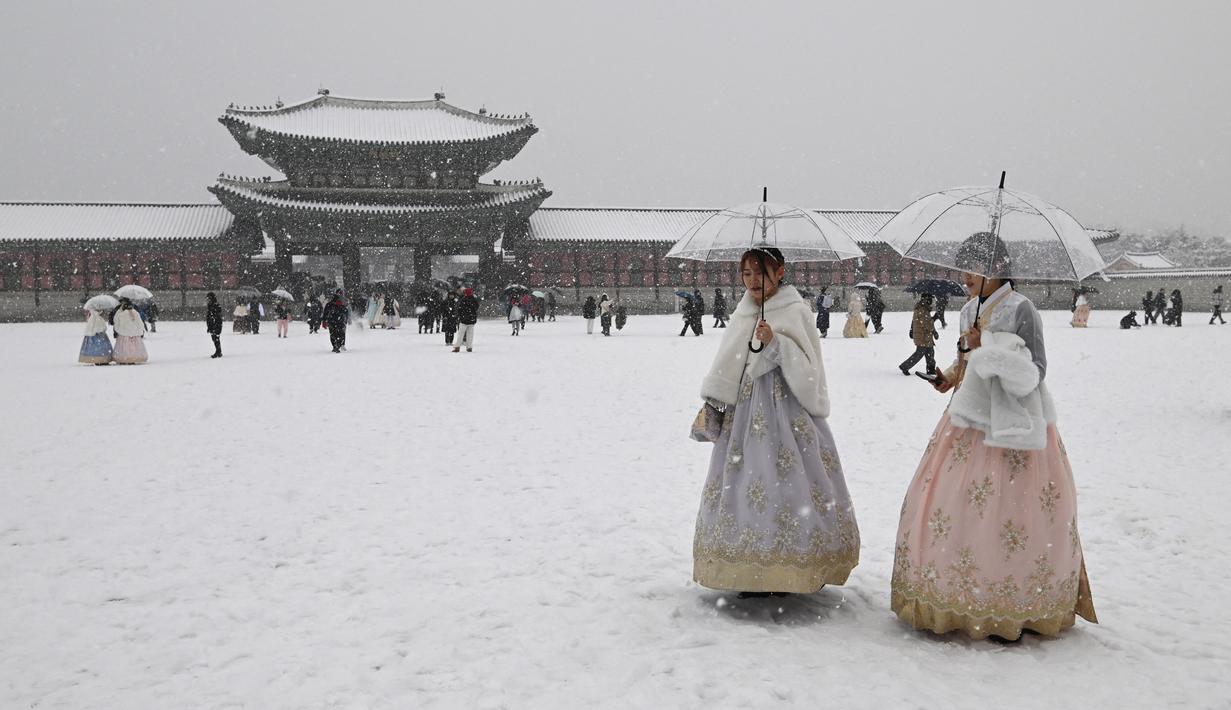 Pengunjung yang mengenakan pakaian tradisional hanbok berjalan di tengah salju di istana Gyeongbokgung di pusat kota Seoul, Korea Selatan, Sabtu (30/12/2023). (Jung Yeon-je / AFP)