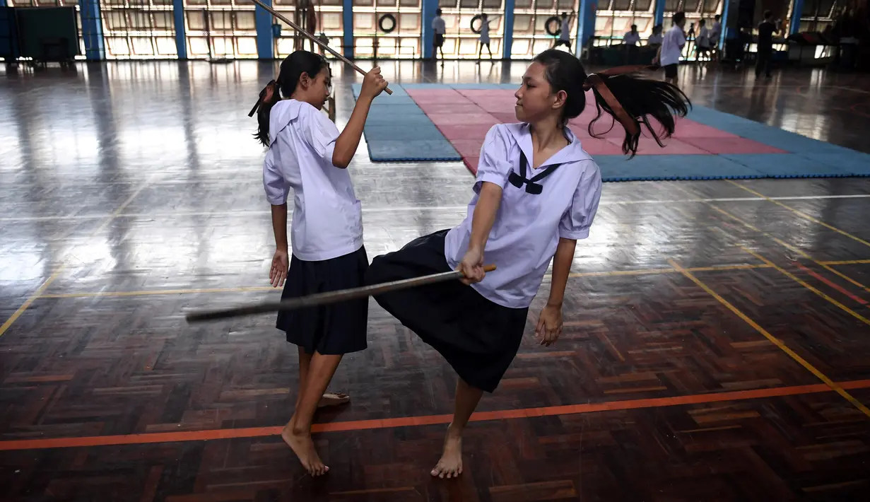 Dua siswi bertarung menggunakan pedang selama berlatih Krabi Krabong di sekolah Thonburee Woratapeepalarak, Thonburi, Bangkok (8/7/2019). Krabi Krabong merupakan seni bela diri Thailand yang dipersenjatai pisau dan perisai kayu. (AFP Photo/Lillian Suwanrumpha)