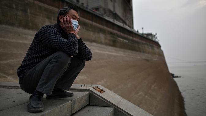 Seorang pria yang memakai masker wajah melihat ke Sungai Yangtze di Wuhan (20/11/2020). Dari total 50.340 kasus yang positif di Wuhan, 3.869 orang telah meninggal dunia akibat Covid-19 dan yang sembuh 46.471 orang. (AFP/Hector Retamal)